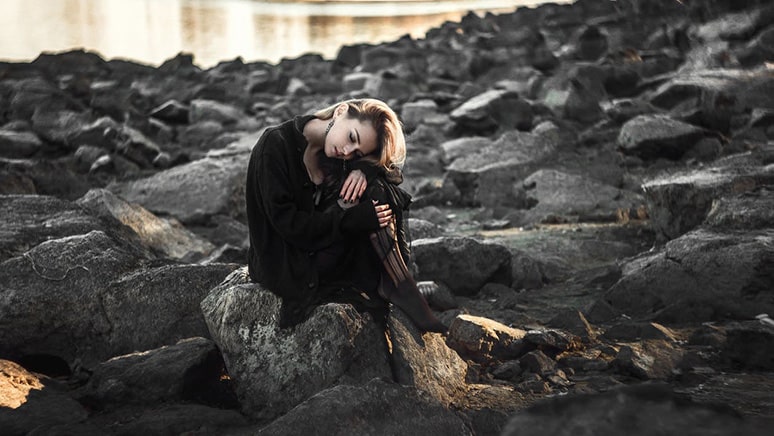Unhappy woman sitting on rock wonders what are the symptoms of anorexia nervosa