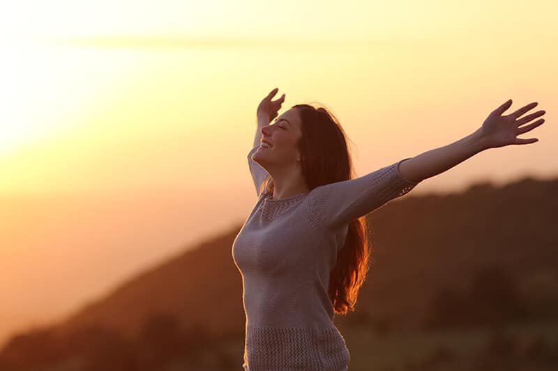 Woman at sunset breathing fresh air raising arms