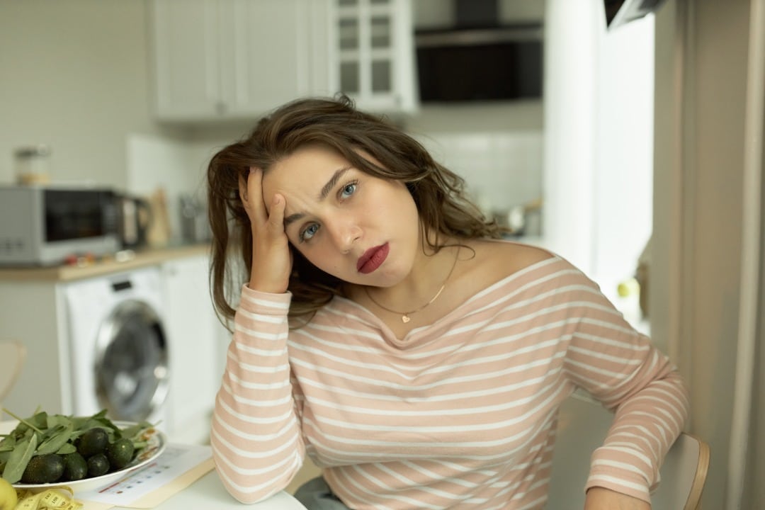 Woman sits in her kitchen and looks stressed.