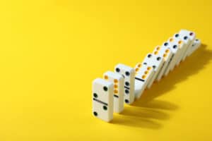 A row of dominoes falling on a bright yellow background.