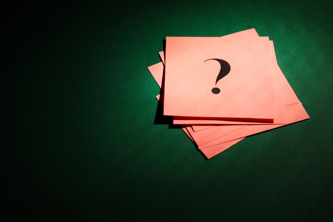 Pink sticky notes with a question mark on them sitting on a dark green background.