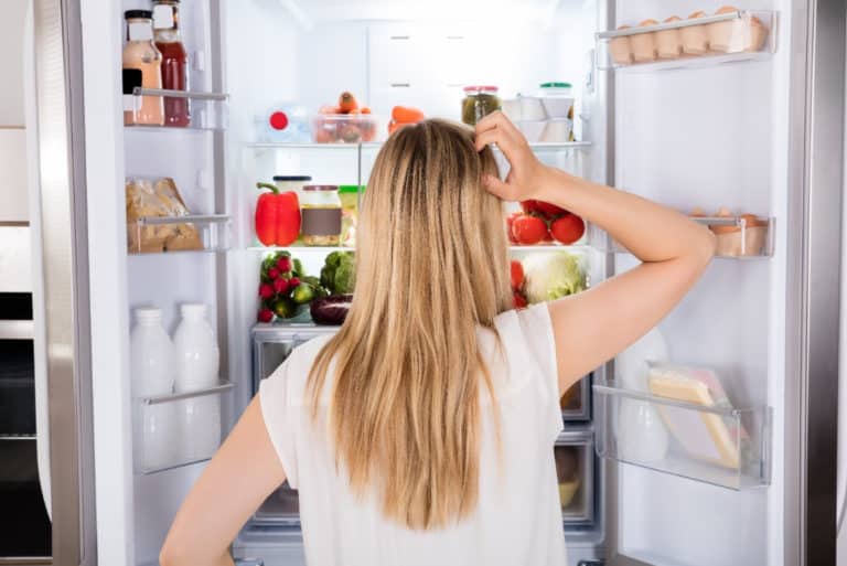 Woman stands in front of an open refrigerator.