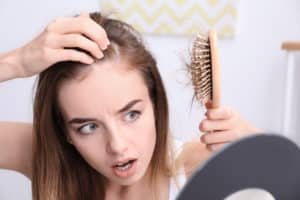 Woman looks in the mirror with a hairbrush surprised by her hair loss.