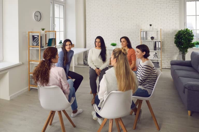 A support group of women gathered in a room and sitting in chairs.